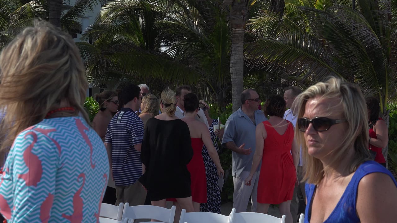 Adults mingling near white chairs under palm trees
