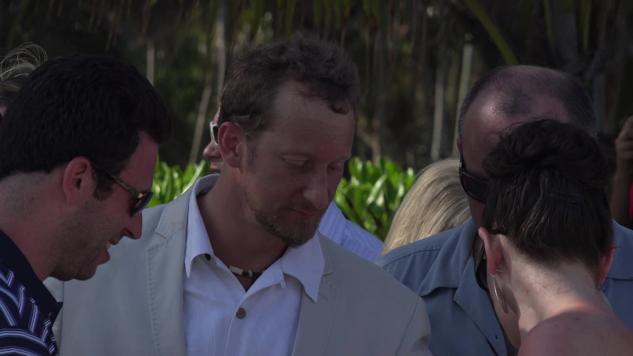 Several adults in a tight outdoor crowd, including men in sunglasses and a woman seen from behind.