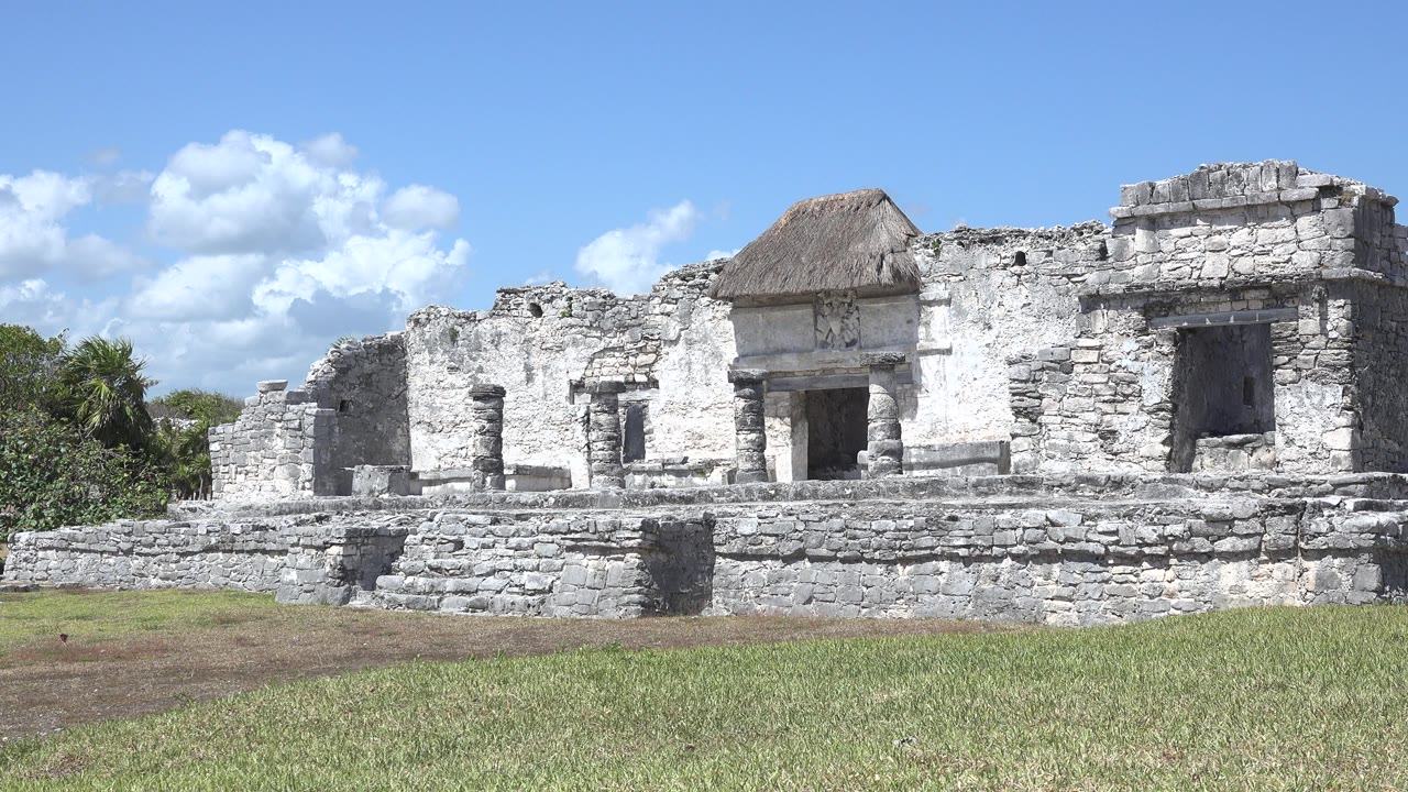 The Tulum ruin remains centered, showing the dark central doorway, low stone steps, rough wall texture, blue sky, and no visible people.