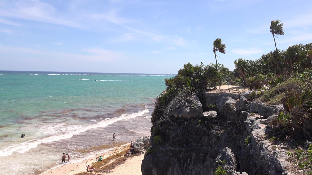 Rocky beach bluff beside turquoise water with people on the sand