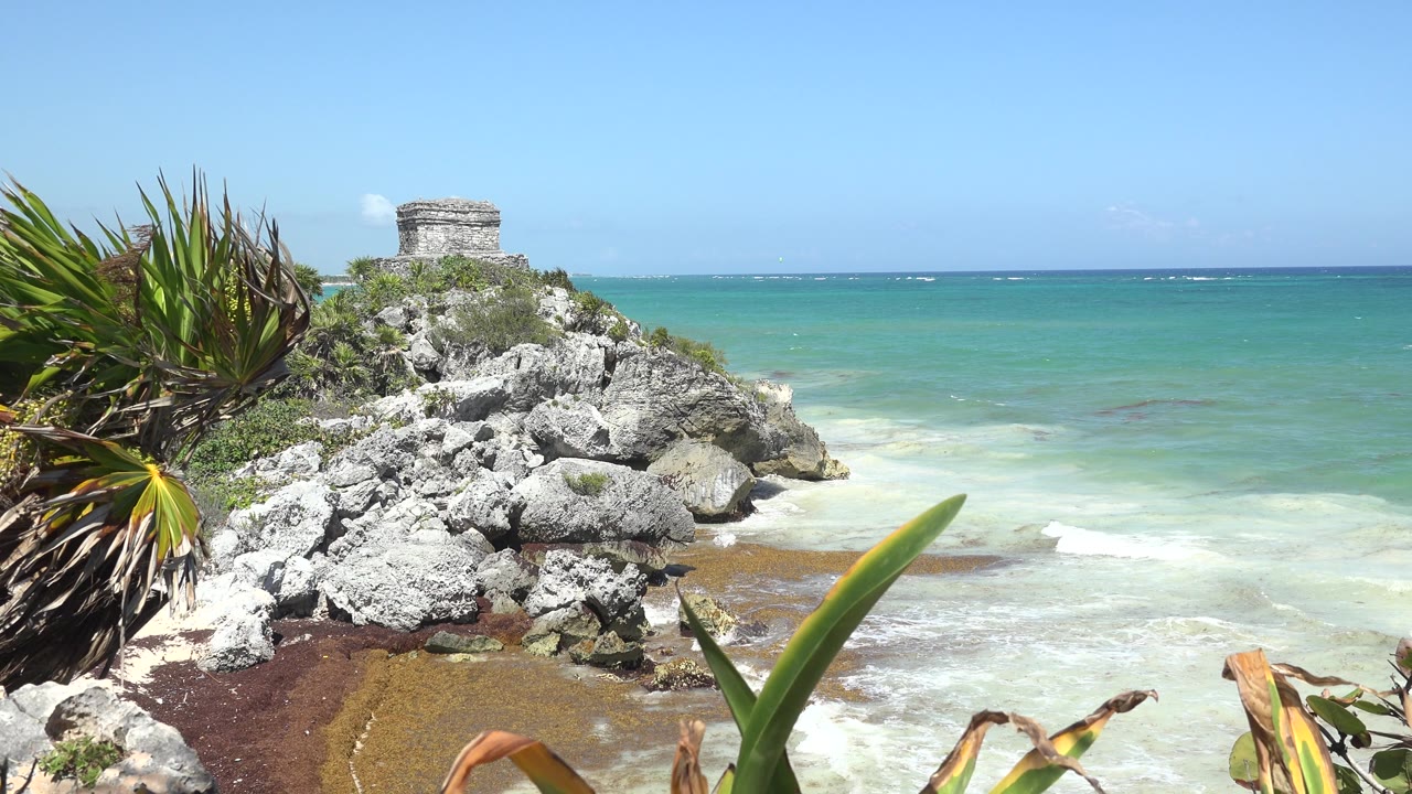 Stone structure on rocks beside blue-green ocean and foamy surf.