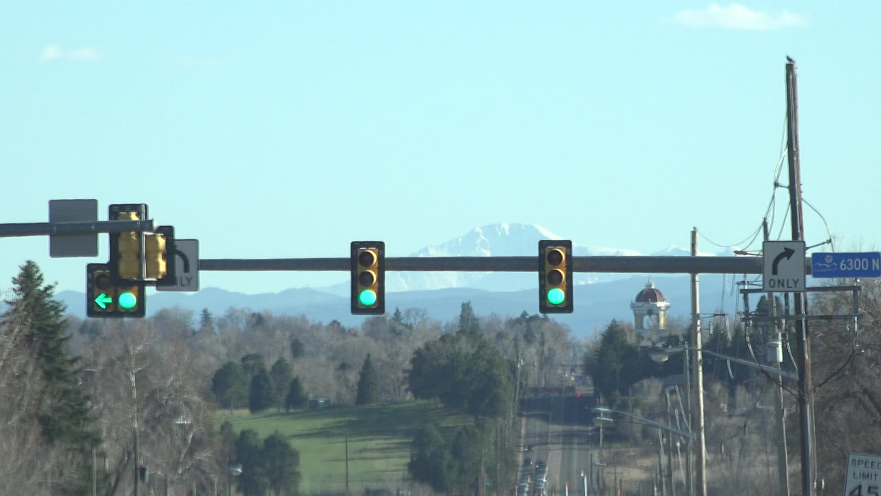 Denver, Colorado road view with green traffic signals, bare trees, distant snowy mountains, utility poles, and no visible people at the start of the clip.