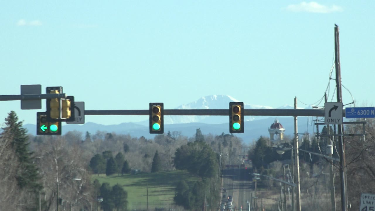 Denver, Colorado street scene with illuminated green signals, a long road corridor, winter trees, distant mountains, and no visible people.