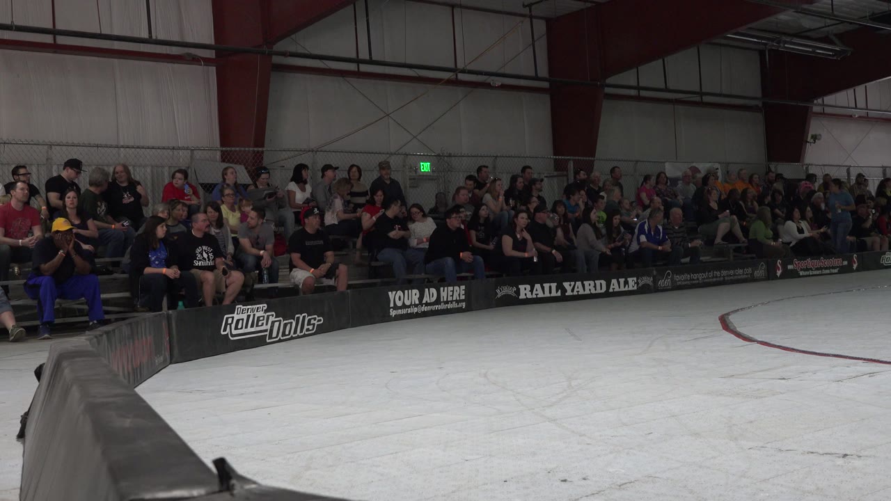 Denver roller derby crowd viewed from rink level, with seated spectators centered above the dark barrier and white track in the foreground.