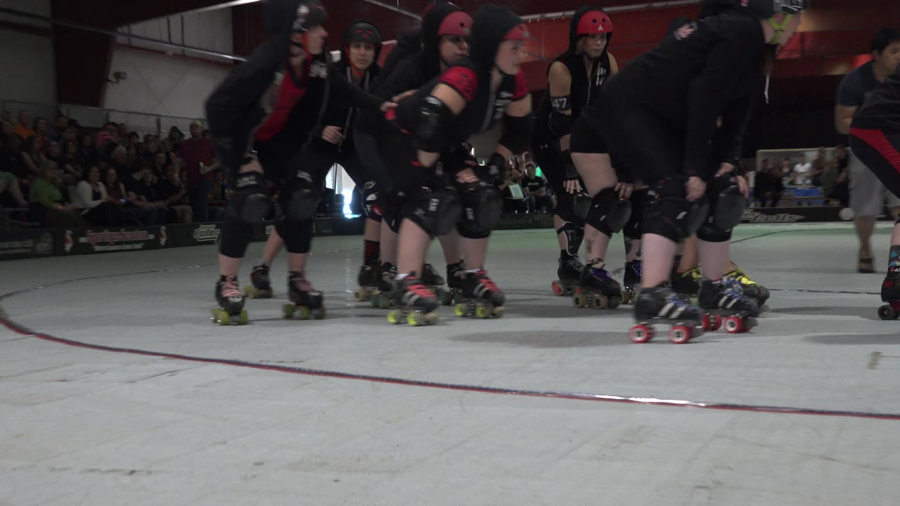 Roller skaters in black gear cluster on an indoor rink.