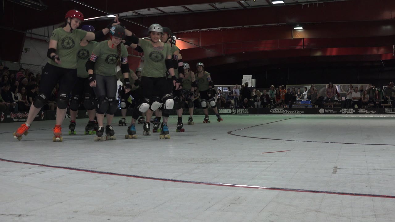 Helmeted skaters in green tank tops roll together on an indoor rink.