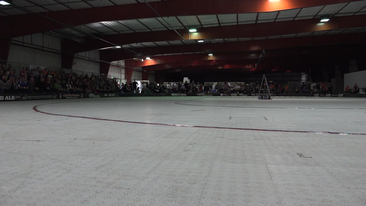 Wide empty roller rink with spectators along the far wall.