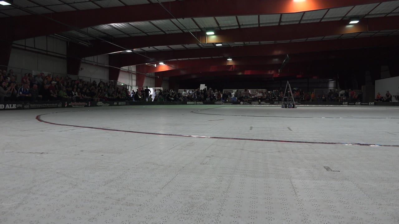 Indoor roller rink floor with spectators and ceiling beams.