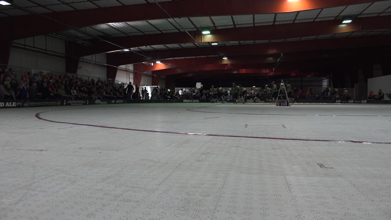The Denver roller derby venue remains in a wide composition with the empty rink foreground, spectators across the back, and a ladder near the right side.