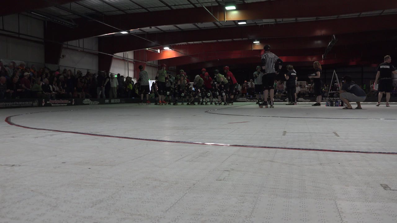 Low view of roller derby athletes gathered on an indoor rink.