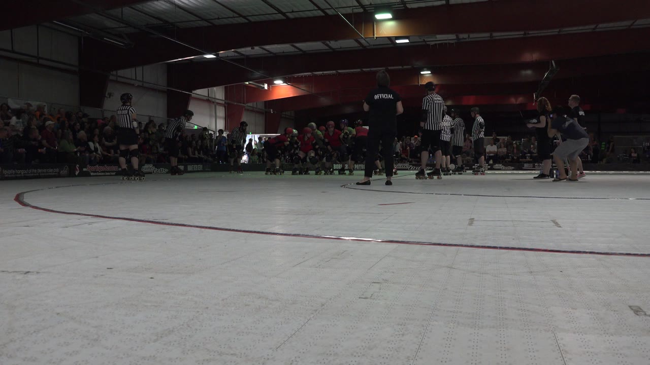 Low-angle roller derby rink with skaters, officials, and bleachers.