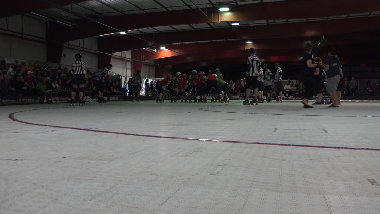 Wide low view of indoor rink with skaters, referees, and spectators.