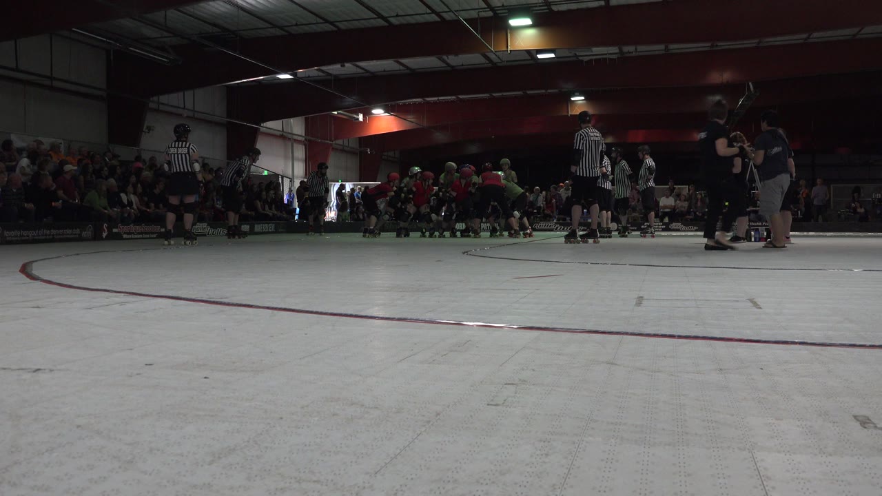 At 0:01 in Denver, Colorado, helmeted skaters gather near the far side of the rink as a striped referee stands near center and spectators sit behind the action.