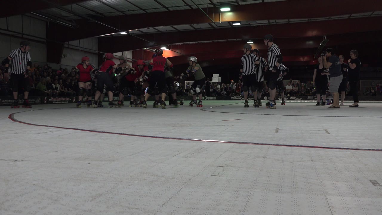 Roller skaters and referees on an indoor rink with spectators in the background.