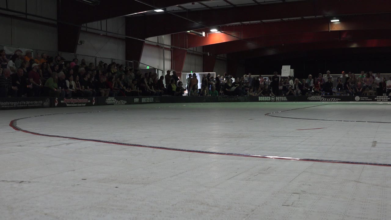 Dim ice rink with spectators seated in dark bleachers.