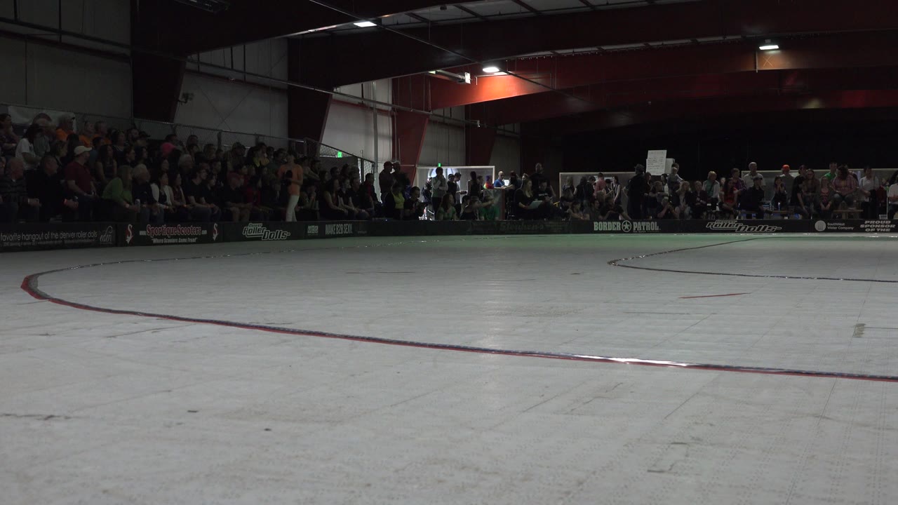 Indoor roller rink with spectators along the far wall.