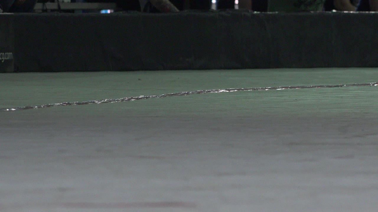 A low ground-camera frame shows the same cracked roller rink floor in Denver, Colorado, with the bright seam running across the foreground and no visible people.