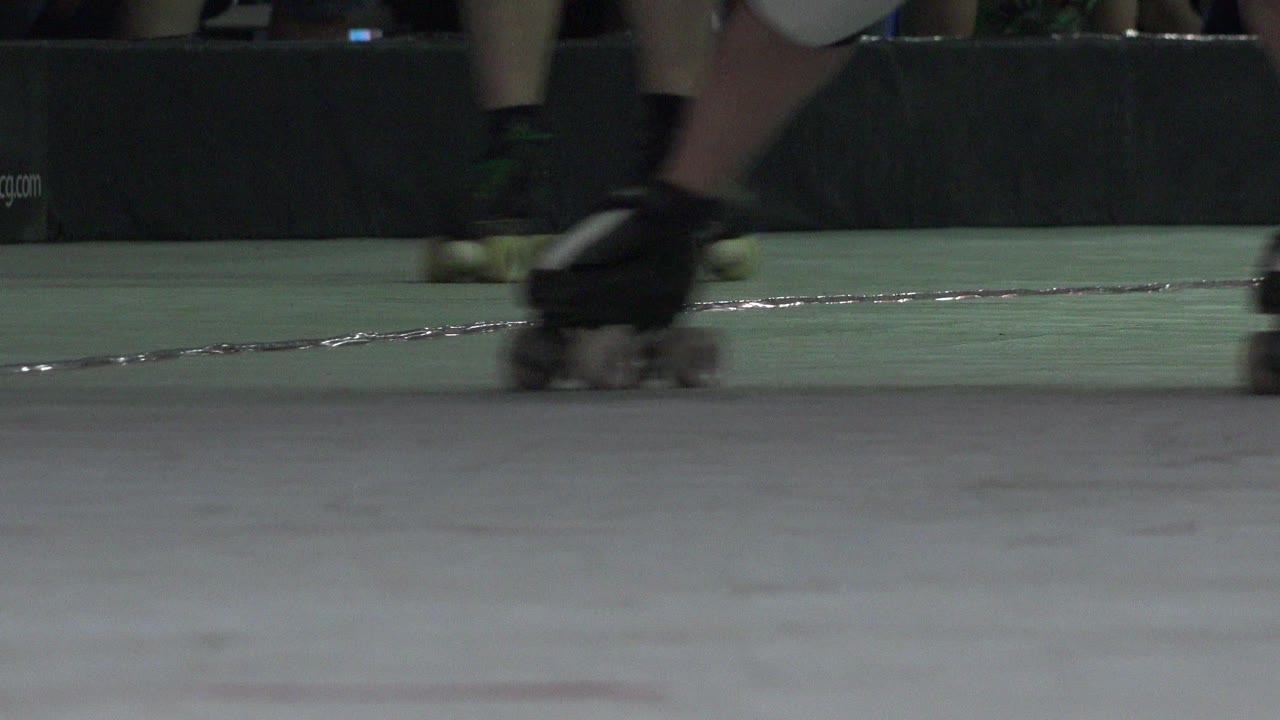Ground-level Denver roller skating frame with skaters' lower legs and quad skates moving across a pale rink floor near a dark barrier.
