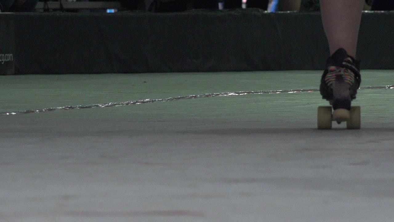A roller skate sits near the lower center of the Denver indoor rink frame, with the floor taking most of the image and a padded wall in the background.