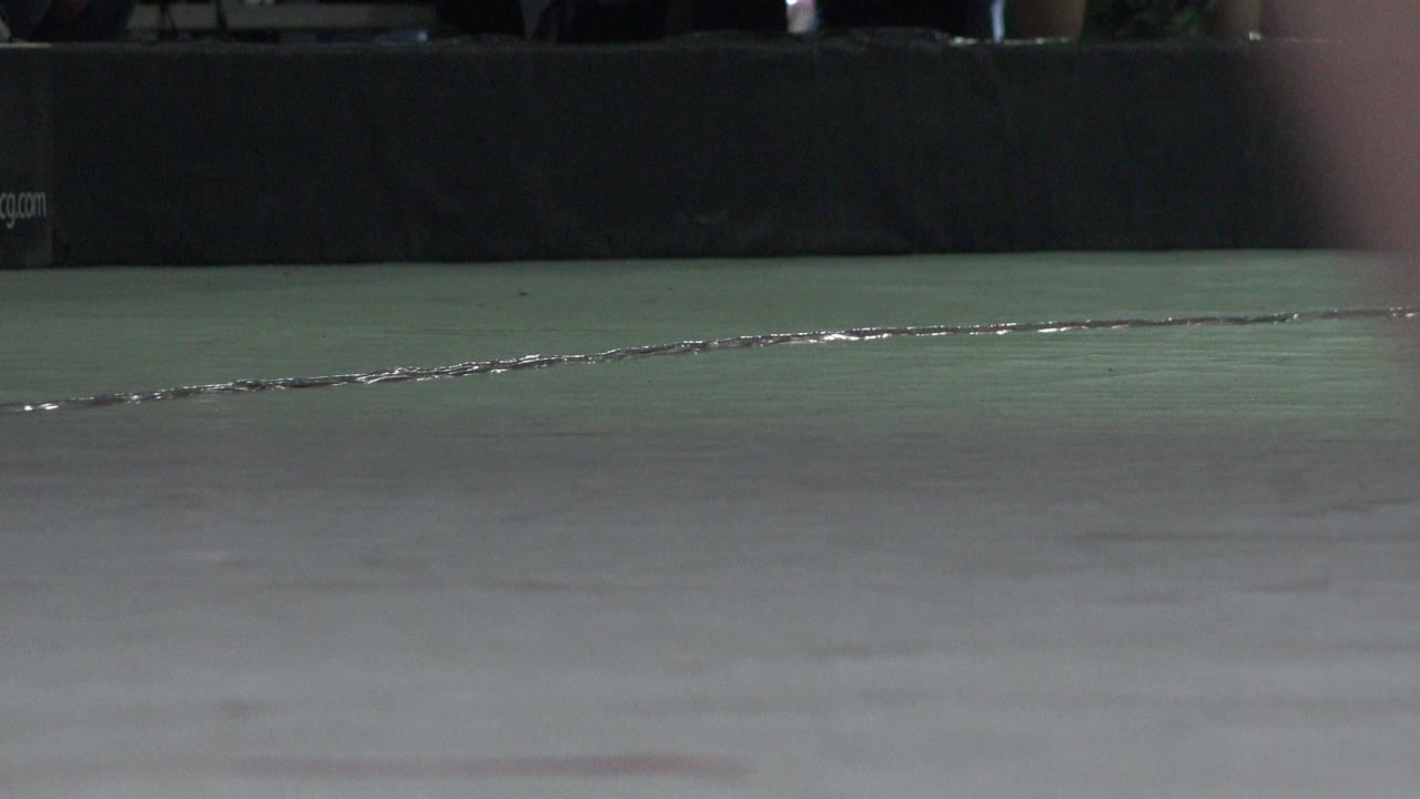 Low view of an indoor rink floor with a dark padded barrier behind it.