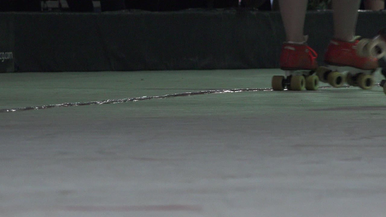 A close low-angle Denver 2015 frame keeps red roller skates near the top edge with a dark padded barrier behind them.