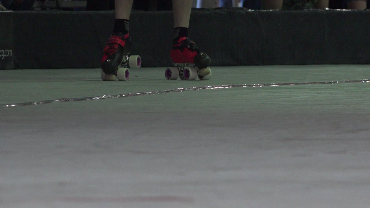 Lower legs in black-and-red quad skates on an indoor floor.