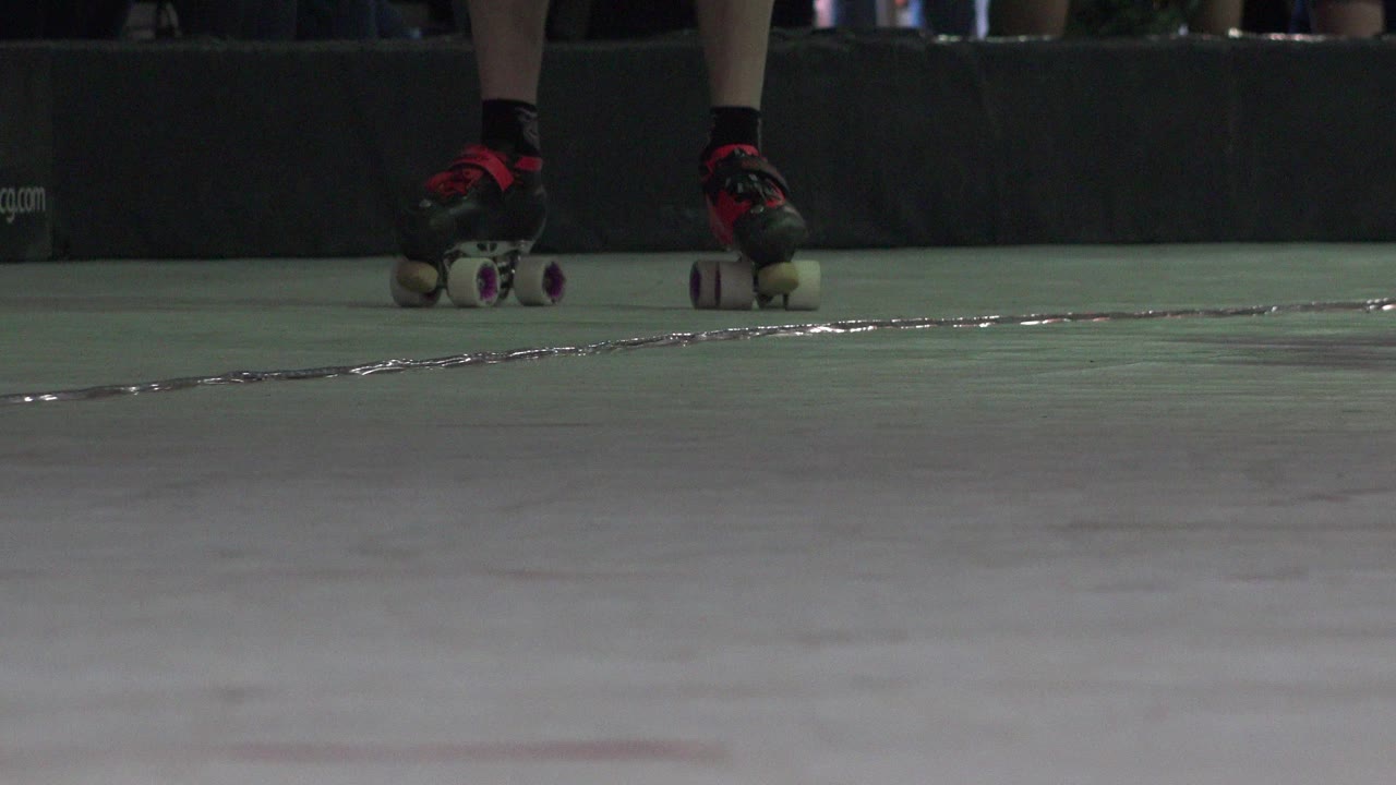 A low Denver 2015 skate detail shows black roller skates with red accents moving along the back edge of the pale floor beside a dark barrier.