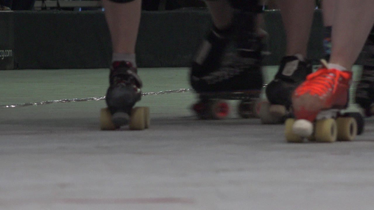 Low-angle roller skates moving across an indoor rink floor.