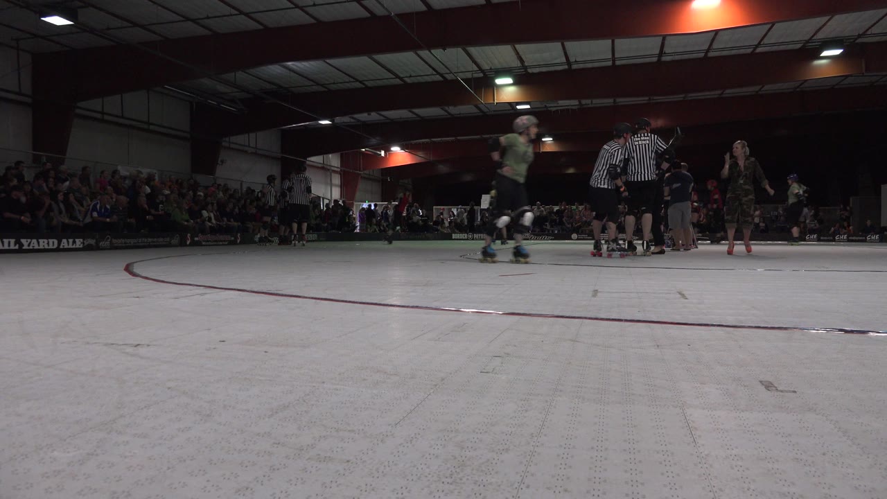 Low indoor rink view with skaters, referees, and spectators.