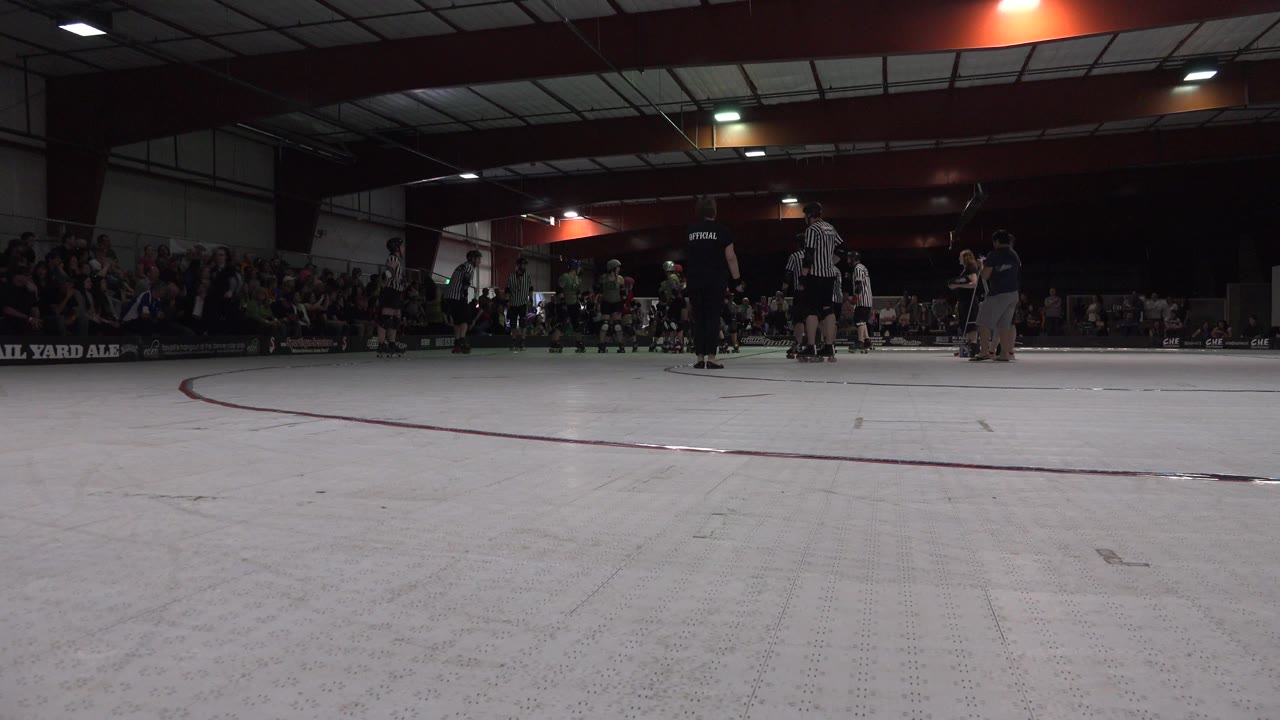 Denver roller derby skaters and referees stand on the rink floor at the start of the clip, with spectators filling the dim stands behind them.