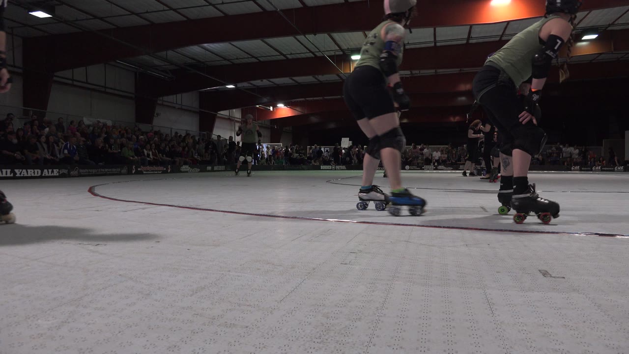 Low rink view of roller derby skaters with spectators in the background.