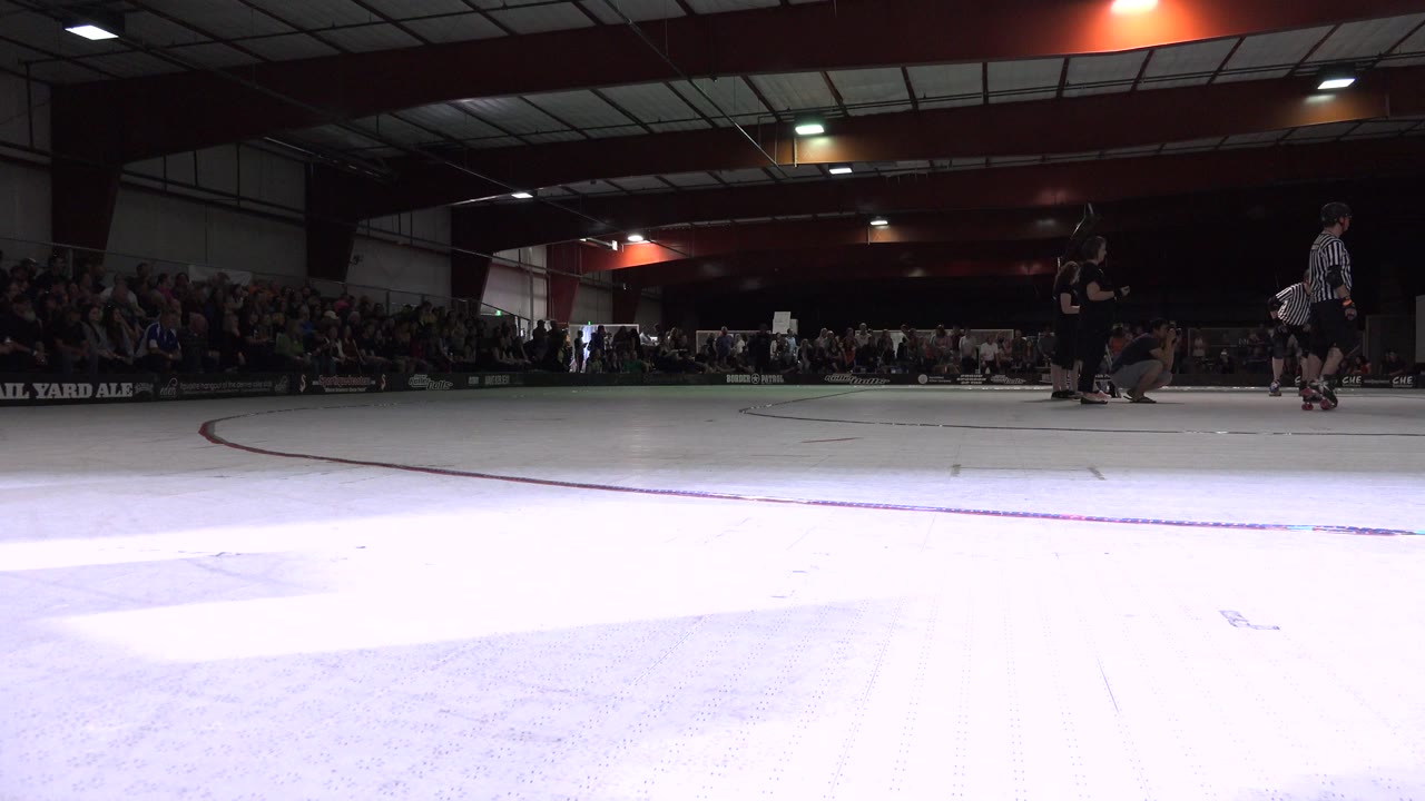 Low view across an indoor roller rink with referees and spectators.