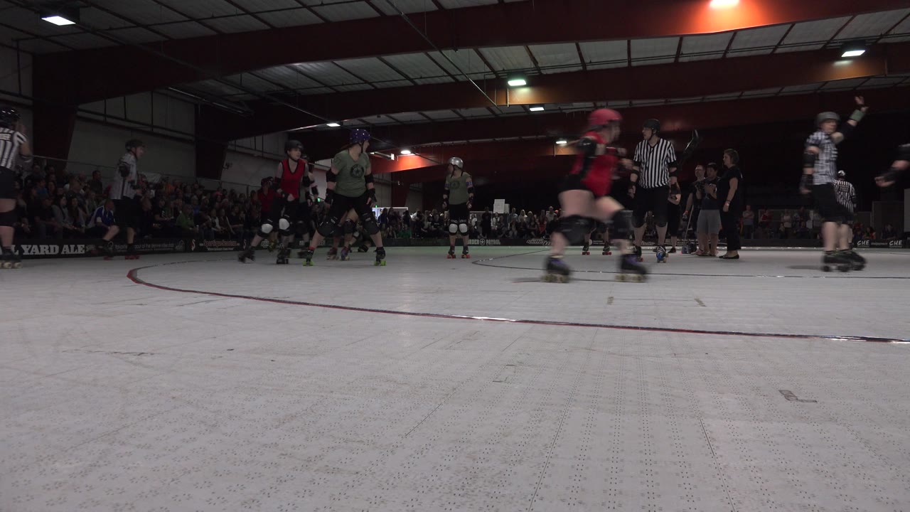 Skaters in helmets move across the right side of an indoor rink.