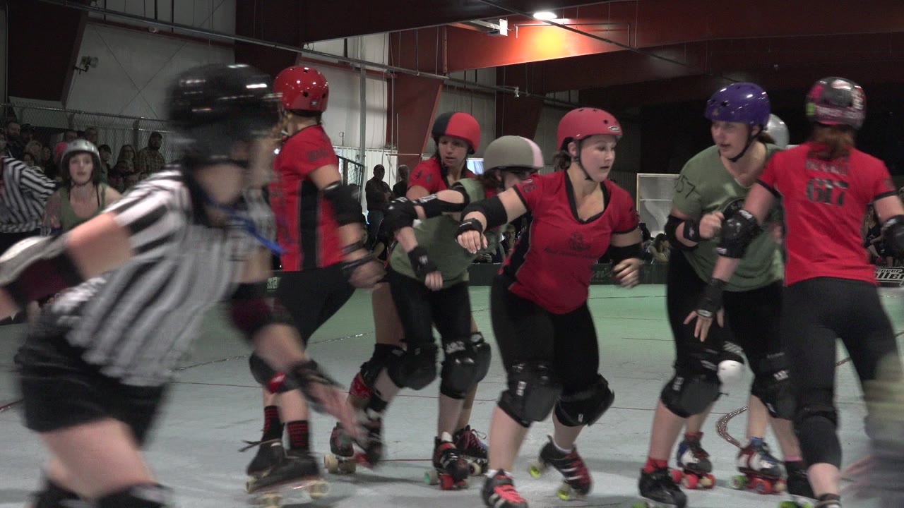 Roller derby skaters and referee on an indoor rink.