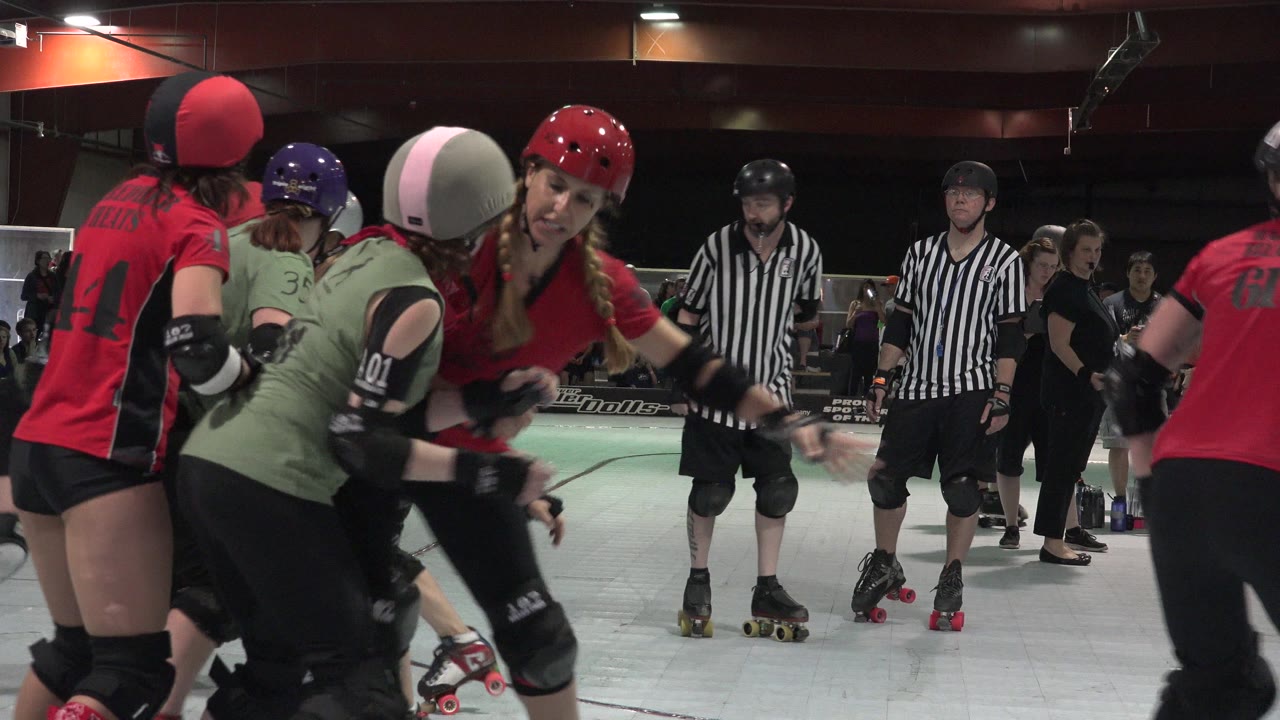 Denver skaters in protective gear lean into each other during a roller derby jam, with two referees and arena spectators visible in the background.