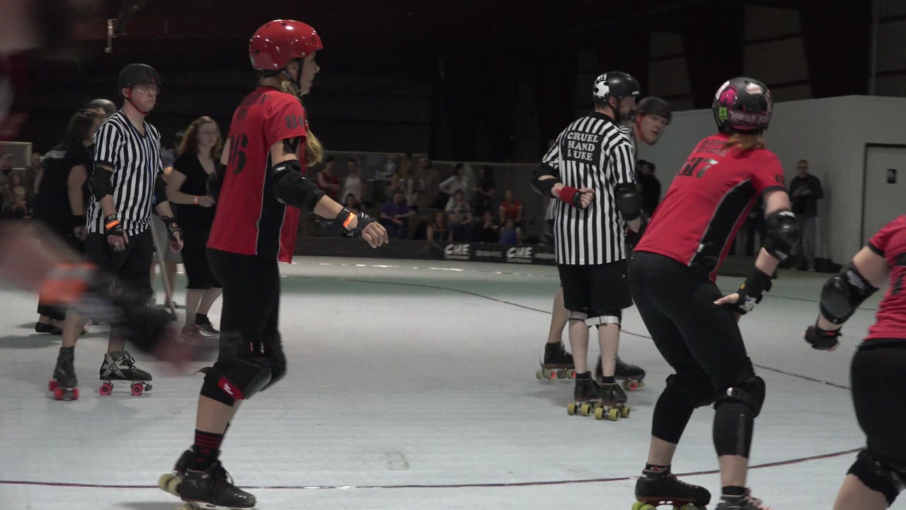 Roller derby players and a referee on an indoor court.