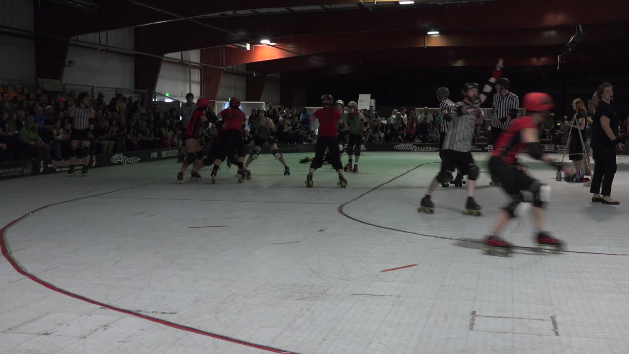 A red skater passes close to camera as the pack and referees remain behind.