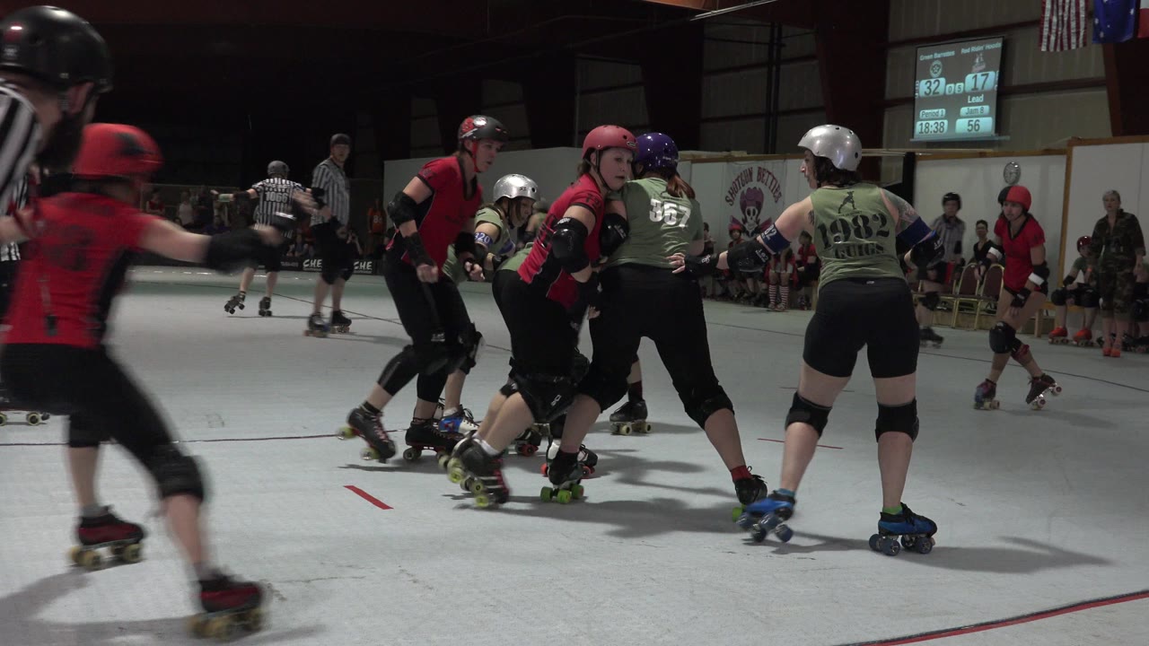 Roller derby skaters cluster near a referee on an indoor rink.