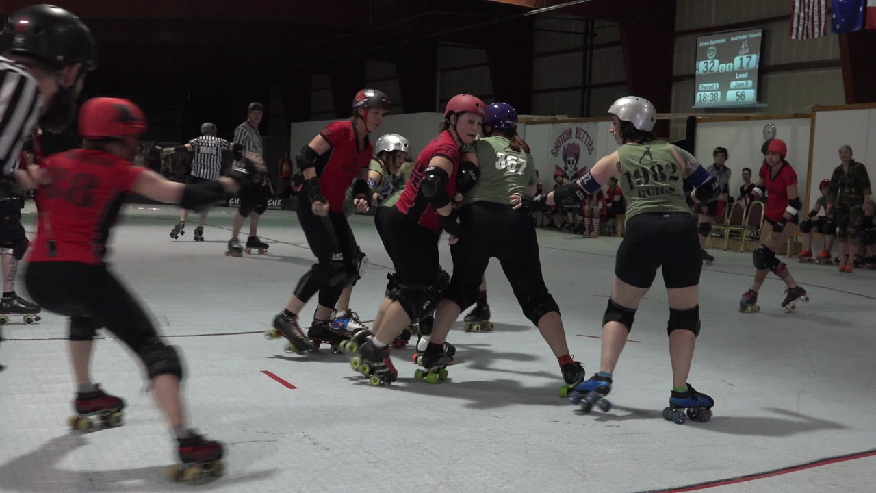 In Denver, Colorado, helmeted skaters circle the indoor rink as red and green players bunch together near the center of the frame.