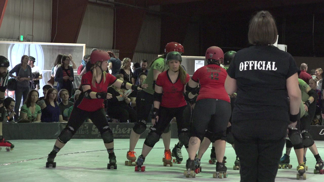 Women on skates line up near an official during an indoor roller event.