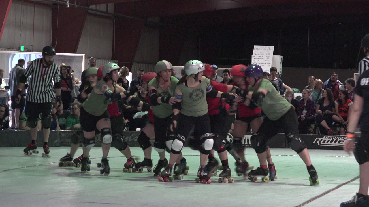 Roller derby players in green and red jerseys cluster near a referee.