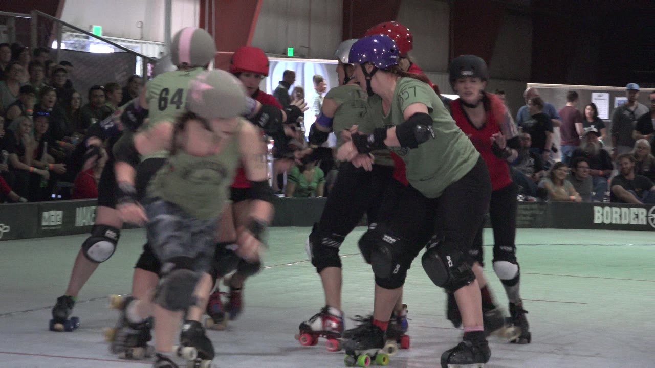 Women roller derby skaters collide near a rink barrier.