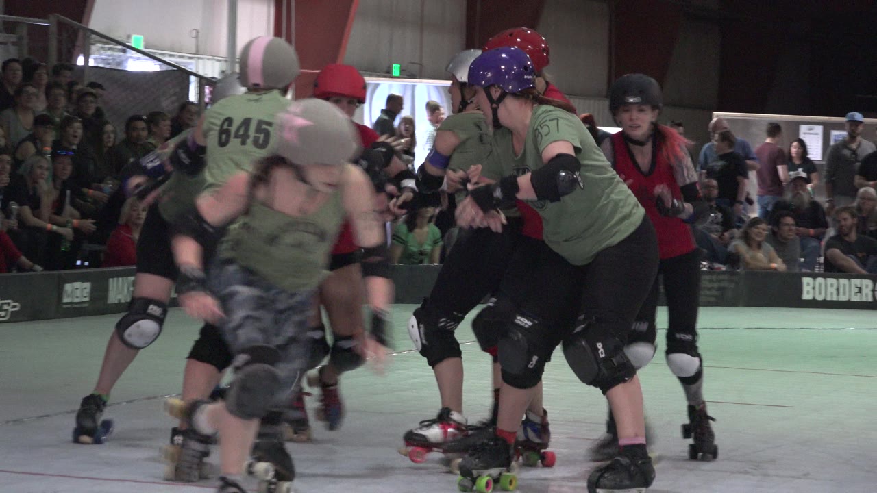 A green-uniformed roller derby skater blurs across the foreground while red and green skaters jostle behind her in the Denver indoor rink.