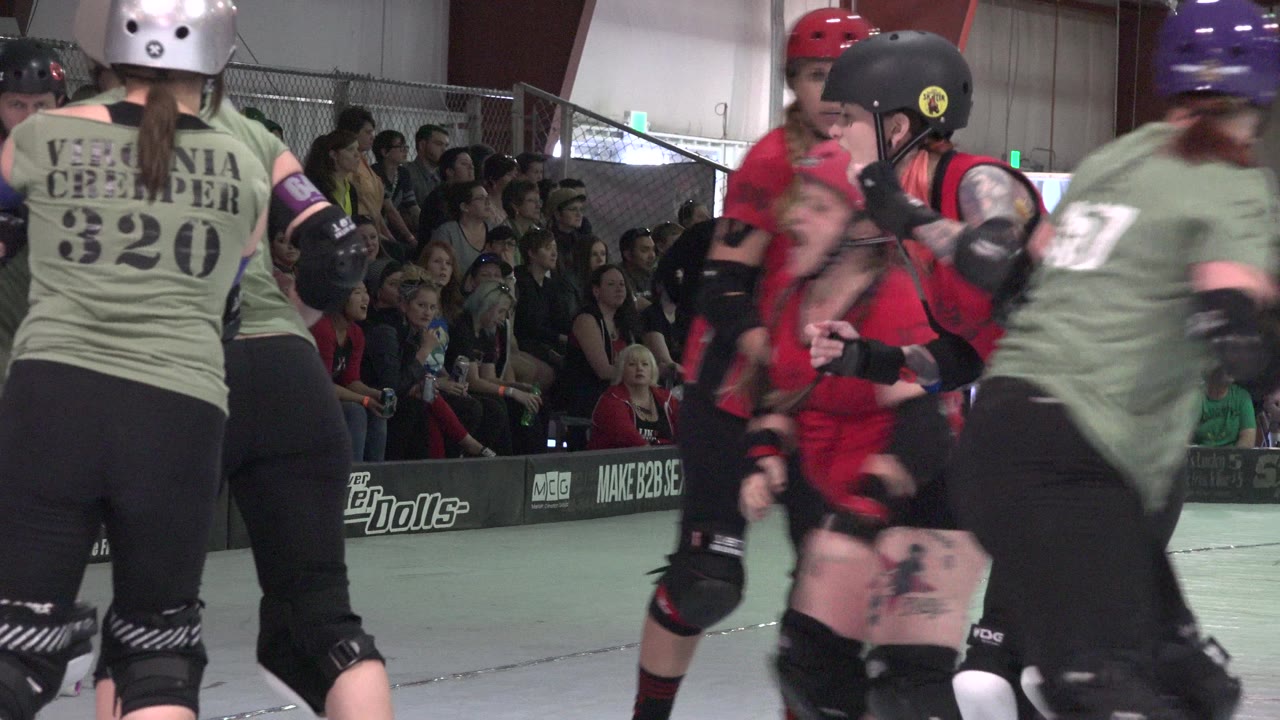 Roller derby skaters in green and red jerseys on an indoor rink.
