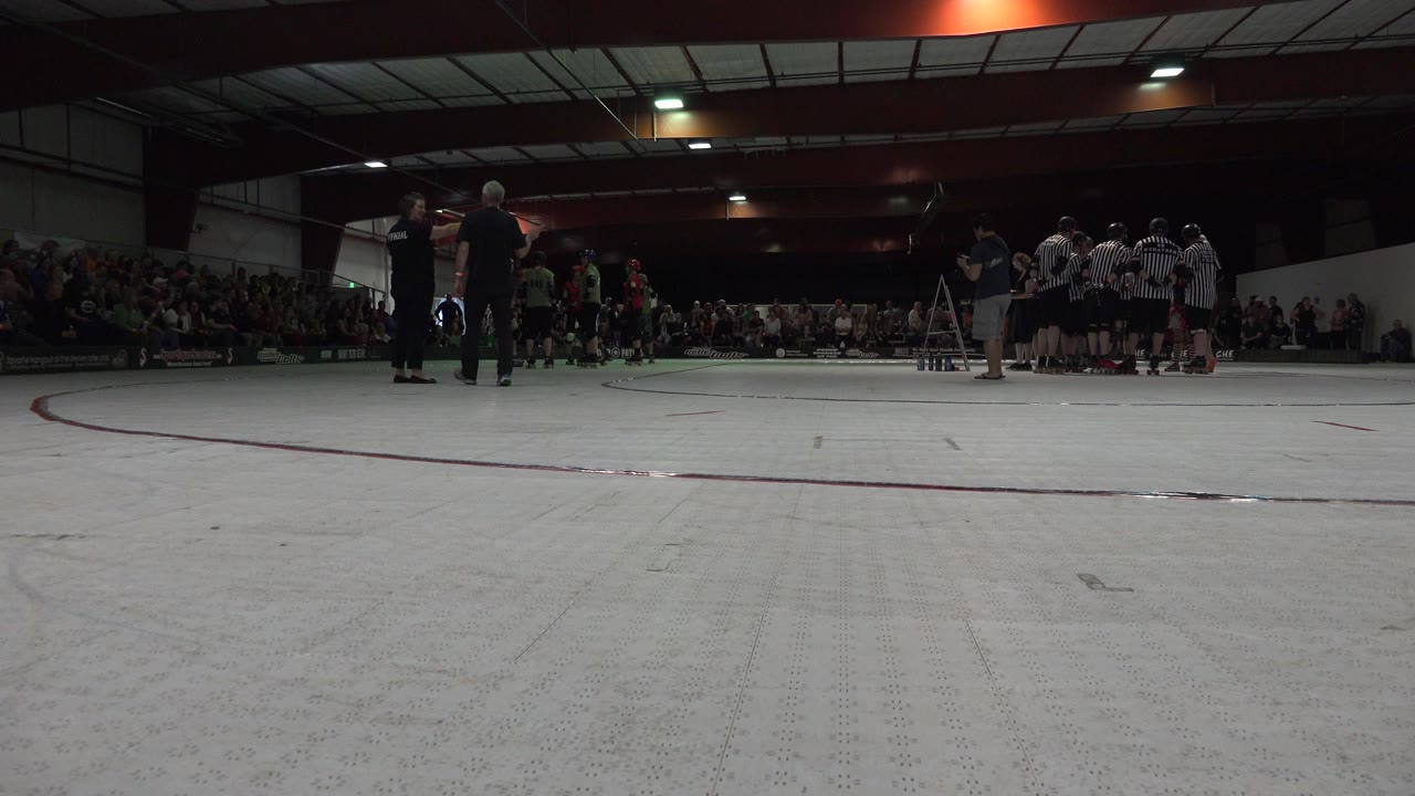 Low view across an indoor rink floor toward people and spectators.