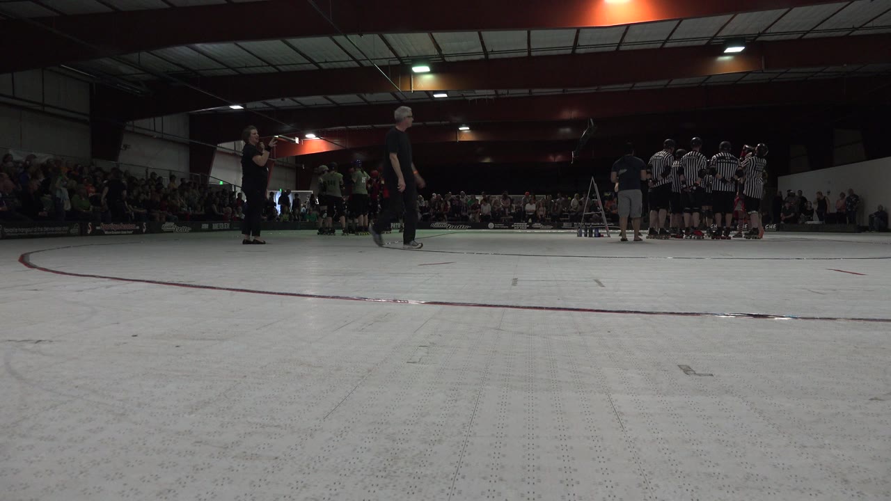 An adult in dark clothing crosses the low foreground while Denver gym spectators and a striped-jersey group remain in the background.