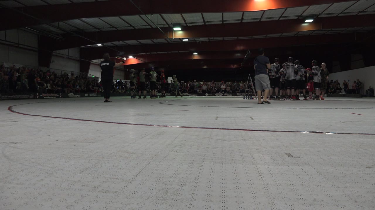 Low view of a white roller derby rink with skaters and spectators in the distance.