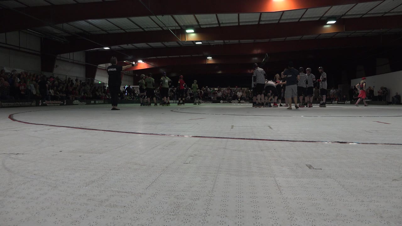 Denver indoor rollerblading scene with teams clustered at the far side of the rink, officials in striped shirts nearby, and a seated crowd lining the background.
