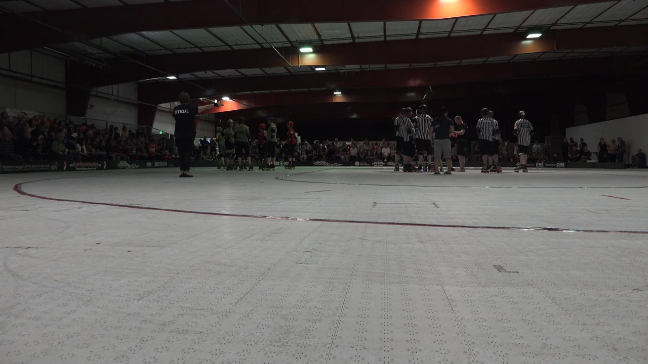 Low view across an indoor skating rink toward rows of skaters and a referee.
