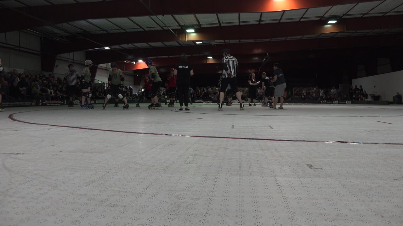 Officials and skaters stand near the audience at an indoor rink.